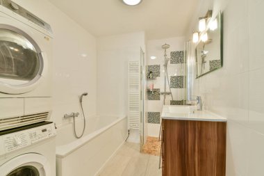 İçinde çamaşır makinesi ve kurutma makinesi, şık bir banyo küveti ve modern aksesuarların olduğu gösterişli bir makyaj malzemesi olan çağdaş bir banyo..