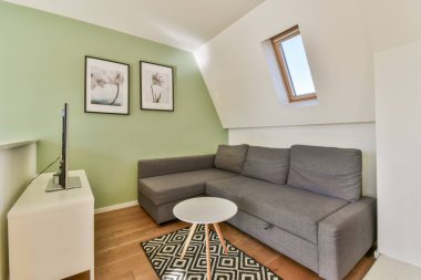 Gri bir kanepe, minimalist dekor, ahşap döşeme ve yeşil aksan duvarlı, rahat bir atmosferi teşvik eden şık bir oturma odası..