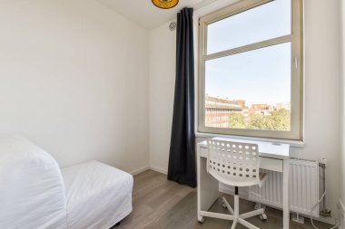 İçinde temiz beyaz bir kanepe olan modern bir iç mekan, pencerenin yanında çalışma masası, doğal ışık ve dışarıdaki yeşilliği gösteren bir bakış..