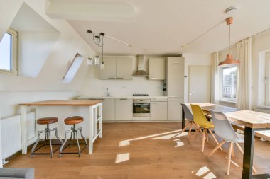 Parlak ve havadar bir modern mutfak, gösterişli bir kabine, ahşap bir yemek masası ve şık bar tabureleri. Doğal ışık çağdaş tasarımı vurgular.
