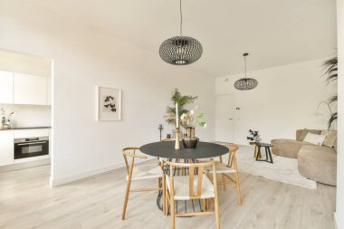 Siyah bir yemek masası, ahşap sandalyeler ve modern dekorun yer aldığı şık, minimalist bir oturma odası huzurlu ve şık bir atmosfer yaratıyor..