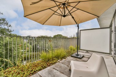 Modern bir balkon, güneş şemsiyesi, rahat bir oturma yeri ve yemyeşil, rahatlamak için davet edici bir açık hava alanı yaratıyor..
