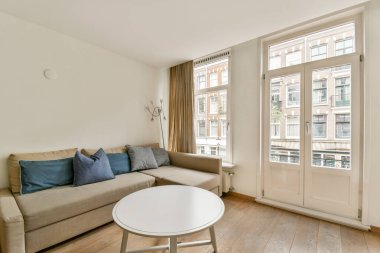 Rahat bir kanepe, dekoratif yastıklar ve doğal ışık ve çağdaş tasarım unsurlarını gösteren geniş pencereli şık bir minimalist oturma odası..