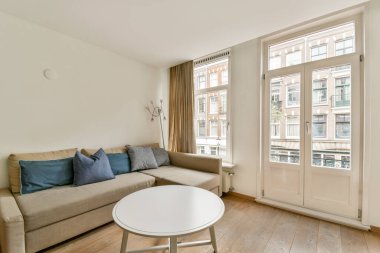 Rahat bir kanepe, dekoratif yastıklar ve doğal ışık ve çağdaş tasarım unsurlarını gösteren geniş pencereli şık bir minimalist oturma odası..