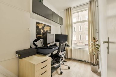 Çift monitörlü minimalist bir ev ofisi, ahşap bir masa ve pencerenin yanında parlak doğal ışık sağlayan dekoratif bir bitki..