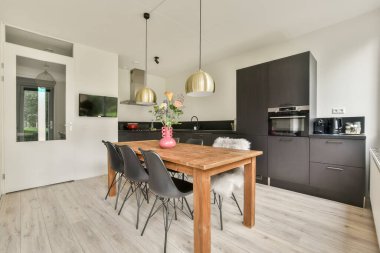 Siyah sandalyeli ahşap bir yemek masası, zarif kolye ışıkları ve çağdaş yaşamı destekleyen şık bir mutfak..