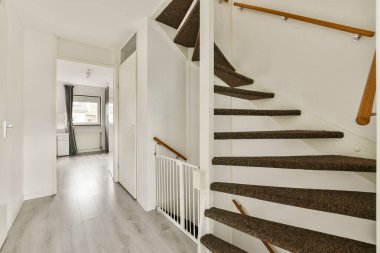 Aydınlatılmış bir iç mekan. Halılı merdivenleri olan modern bir merdiven. Açık renkli duvarları ve rahat bir atmosferi olan davetkar bir koridora açılıyor..