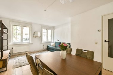 Ahşap bir yemek masası, şık sandalyeler ve minimalist dekor elementleri ile sıcak ve davetkar bir atmosfer yaratan parlak ve havadar bir iç mekan..