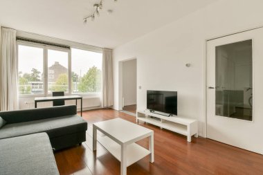 Modern mobilyaların, geniş pencerelerin, doğal ışığın ve çağdaş yaşam için mükemmel ahşap zeminin bulunduğu şık ve şık bir oturma odası..