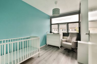 Beyaz bir beşik, yumuşak gri bir sandalye ve bebek için konfor ve sükunet için tasarlanmış yatıştırıcı mavi duvarlar içeren şık bir kreş..