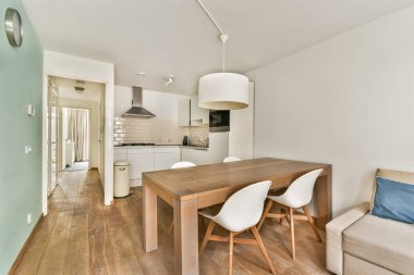 Parlak, modern bir mutfak ve yemek odası. Ahşap döşeme, şık bir yemek masası ve yumuşak ışıklandırma altında modern mobilyalar..