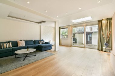 Konforlu bir kanepe, ahşap döşeme ve doğal ışığın bölgeyi aydınlatmasına olanak sağlayan geniş ve şık bir oturma odası..