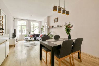 Şık, modern bir oturma odası yemek odası, parlak doğal ışık ve dekoratif bitkiler, sıcak ve davetkar bir atmosfer yaratıyor..