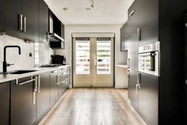 Karanlık dolaplar, paslanmaz çelik aletler ve ahşap zemin içeren gösterişli, modern bir mutfak tasarımı. Yerleşim alanı ve işlevselliği maksimuma çıkarır.