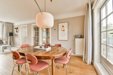 Zarif sandalyeler, yumuşak ışıklandırma ve davetkar atmosferi yükselten zarif dekorlarla çevrili yuvarlak ahşap bir masa içeren çağdaş bir yemek odası..