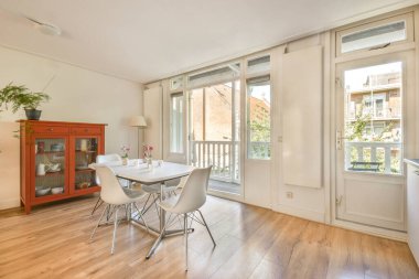 Modern masa ve sandalyelerin yanı sıra şık bir depo ve doğal ışık için geniş pencereler içeren parlak ve davetkar yemek alanı.