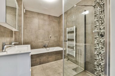 Gösterişli ve çağdaş bir banyo. Lüks bir cam duş, şık eşyalar ve rahatlatıcı bir ortam yaratan zarif fayanslar..