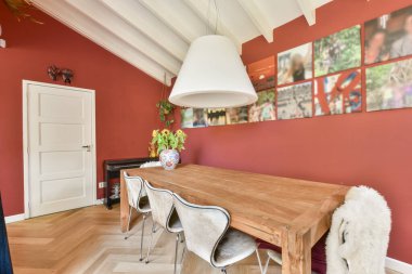 Uzun ahşap bir masa, parlak sandalyeler ve duvarlarda canlı sanat eserlerinin yer aldığı şık bir yemek odası, çağdaş tasarım ve dekor sergileniyor..