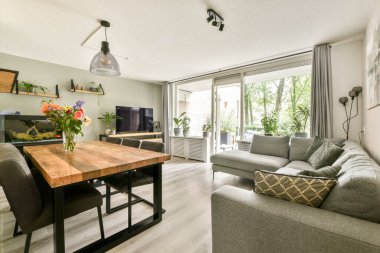 Şık bir yemek masası, rahat bir kanepe ve uzaya hayat veren yemyeşil bitkilerin bulunduğu çağdaş bir oturma odası..