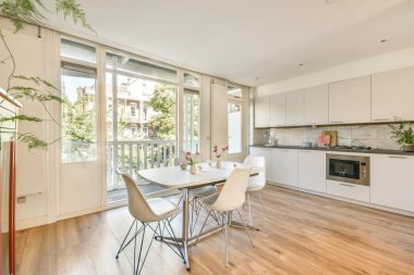 Yemek salonu olan şık bir mutfak. Doğal ışık getiren büyük pencereler var. Yemekler için mükemmel bir karşılama ve havadar atmosfer yaratıyor..