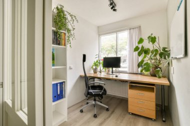 Ahşap bir masa, bir bilgisayar kurulumu ve bereketli kapalı alan bitkilerinin yer aldığı iyi organize edilmiş bir ev ofisi, huzurlu bir çalışma alanı atmosferi yaratıyor..