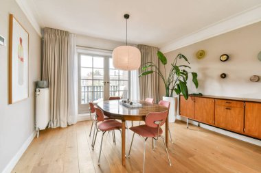 Yuvarlak bir masa, ahşap sandalyeler ve modern dekor elementlerinin yer aldığı şık bir yemek alanı. Yemekler ve toplantılar için sıcak ve davetkar bir atmosfer sunuyor..