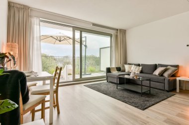 Konforlu bir bölüm kanepesi, cam bir masa ve bahçeye bakan geniş pencereli çağdaş bir oturma odası. İç tasarım konfor ve stili birleştirir..