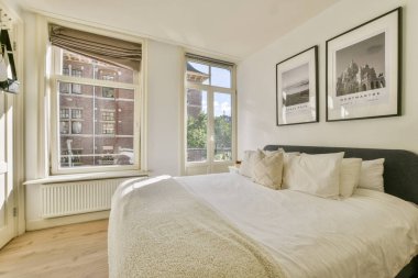 Doğal ışık sağlayan, rahat bir yatak odası ve şık duvar sanatıyla süslenmiş zarif bir dekorun sergilendiği çağdaş bir yatak odası..