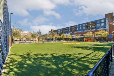 Canlı bir şehir parkında yemyeşil çimenler, düzgün budanmış ağaçlar ve arka planda dinlenmek ve dinlenmek için mükemmel modern binalar var..