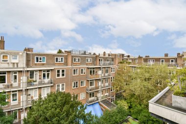 Canlı bir şehir manzarası. Yeşilliklerle çevrili konutları gösteriyor. Doğa ve şehir yaşamı arasındaki zıtlığı vurguluyor..