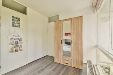 İyi ışıklandırılmış, minimalist bir yatak odası. Ahşap bir gardırop ve pürüzsüz döşeme, davetkar bir atmosferde çağdaş tasarım unsurlarını ön plana çıkarıyor..