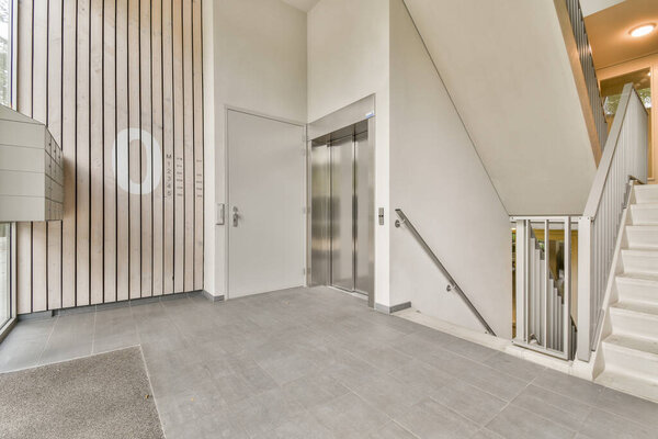 Элегантный и современный интерьер с лестницей рядом с лифтом. Дизайн отличается минималистской эстетикой с чистыми линиями и нейтральными цветами.