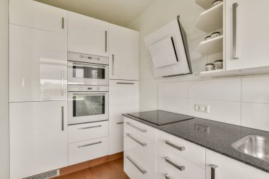 Beyaz dolapların, paslanmaz çelik aletlerin ve şık bir tezgahın olduğu şık, modern bir mutfak. Çağdaş ev dekorasyonu için mükemmel..