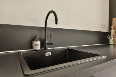 Parlak, siyah bir mutfak lavabosu çağdaş bir tezgaha entegre edilmiş, minimalist stil ve işlevsellik sergiliyor. Modern mutfak estetiği için mükemmel..