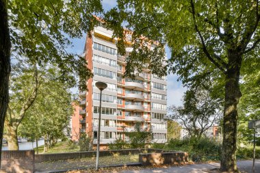 Çağdaş bir apartman dairesi, yemyeşil ağaçlarla çerçevelenmiş, kentsel yaşamı doğayla uyum içinde gösteren..