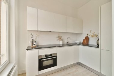 Beyaz dolaplar, şık bir tezgah ve minimalist estetiği geliştiren basit dekor unsurları içeren gösterişli ve çağdaş bir mutfak tasarımı..