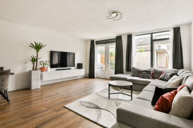Lüks koltuklar, çağdaş bir TV kurulumu ve geniş pencerelerden süzülen doğal ışığın bulunduğu şık bir oturma odası rahat ama modern bir atmosfer sunuyor..