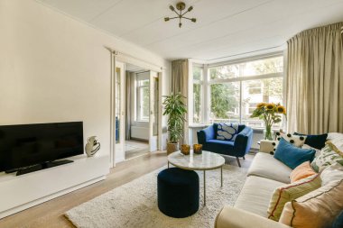 Rahat mobilyaların, büyük pencerelerin ve kapalı alandaki bitkilerin karışımından oluşan şık, modern bir oturma odası, sıcak ve davetkar bir atmosfer yaratıyor..