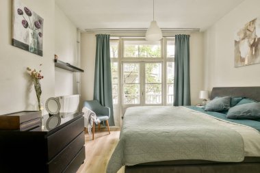 Geniş pencerelerden süzülen, rahat bir atmosfer için şık dekorlar ve yumuşak yatak örtüsüyle tamamlanmış, huzurlu bir yatak odası..