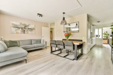 Gri bir kanepe, minimalist bir dekor ve modern bir mutfağa kusursuz bir şekilde bağlanan bir yemek alanı olan gösterişli ve davetkar bir yaşam alanı..