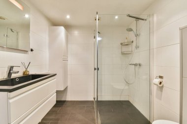 Geniş cam bir duş, parlak bir kibir ve çağdaş fayans döşeme, modern estetik ile karıştırıcı işlevsellik içeren iyi tasarlanmış bir banyo..