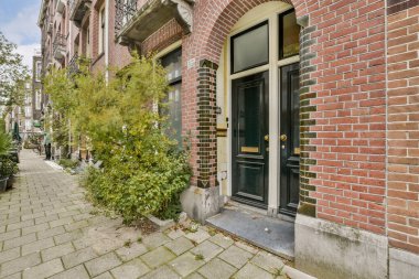 Cazibesini artıran yemyeşil ve kaldırım taşı yolları eşliğinde şık bir girişe sahip bir tuğla cephesinin pitoresk görüntüsü.