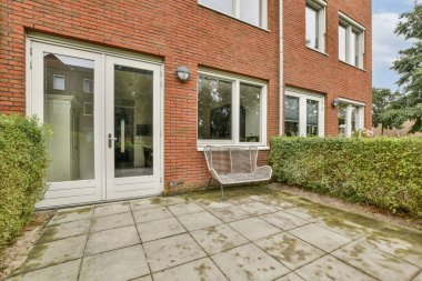 Geniş pencereli çağdaş bir tuğla bina ve içinde oturma alanı ve yeşillik bulunan düzgün bakımlı bir bahçe alanı..