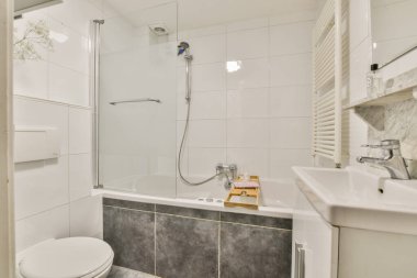 Küvet, duş, parlak lavabo ve modern aksesuarların bulunduğu şık ve çağdaş bir banyo, temizliği ve işlevselliği vurguluyor..