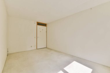 Beyaz duvarlar ve basit bir kapı sergilenen boş bir odanın minimalist görüntüsü, iç tasarımın genişliğini ve basitliğini vurguluyor..