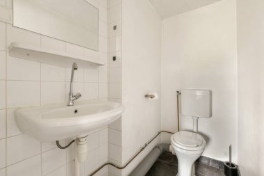 Lavabosu, tuvaleti ve fayanslı duvarları olan temiz ve minimalist bir banyo tasarımda basitlik ve işlevselliği vurguluyor..