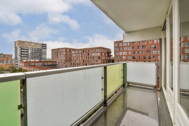 Bir apartman kompleksinin çağdaş balkonunda, berrak mavi gökyüzüne karşı modern binalarla dolu canlı bir şehir manzarası sergileniyor, sakin bir şehir atmosferi yaratıyor..