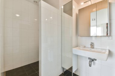 Bu resimde zarif beyaz fayanslara ve şık bir lavaboya sahip gösterişli ve çağdaş bir banyo var. Geniş havasını ve temizliğini arttırıyor..