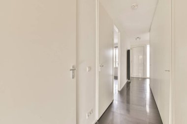 Pürüzsüz, minimalist bir koridor. Temiz çizgiler ve tarafsız renkler sergiliyor. Arka kapıdan gelen ışıkla aydınlatılıyor..