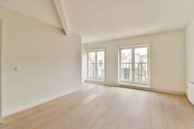 Parlak ve havadar modern bir oda. Dışarıya bakan geniş pencereler var. Ahşap döşeme minimalist alana sıcaklık katar..